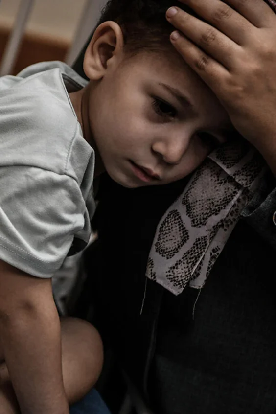 Ein Bub mit einem amputierten Bein liegt in den Armen seiner Mutter.